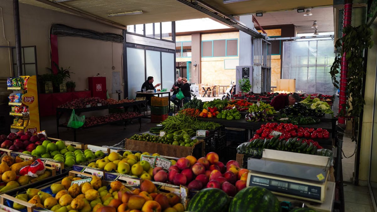 Indoor market showcasing a colorful array of fresh fruits and vegetables with customers in the background.